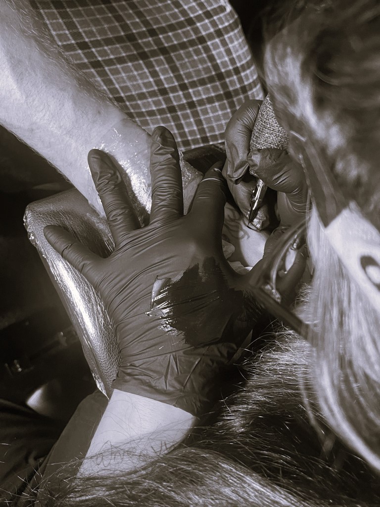 Close-up of Tattoo Mercé using a tattoo machine, focusing on detailed linework on a client’s arm.